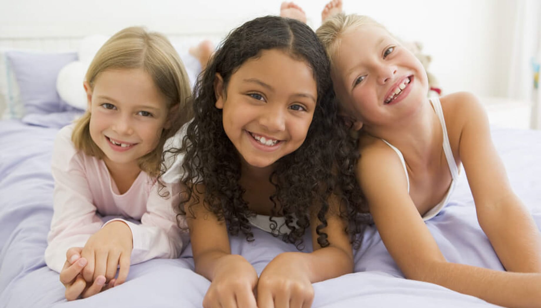Three girls smiling at the camera and getting ready for a slumber party.